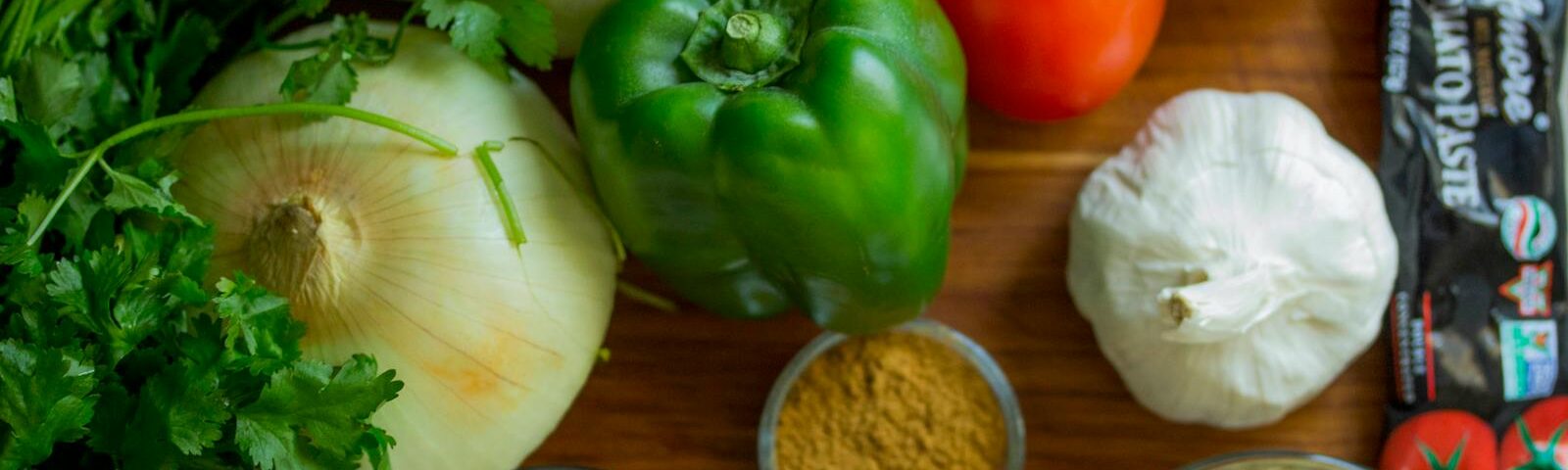 An assortment of fresh vegetables and spices on a wooden table for healthy cooking.