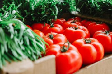 Vibrant red tomatoes and fresh greens displayed at a London farmer's market, showcasing organic produce.