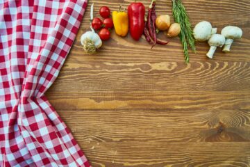 Fresh vegetables and spices on a rustic wooden table with checkered cloth.