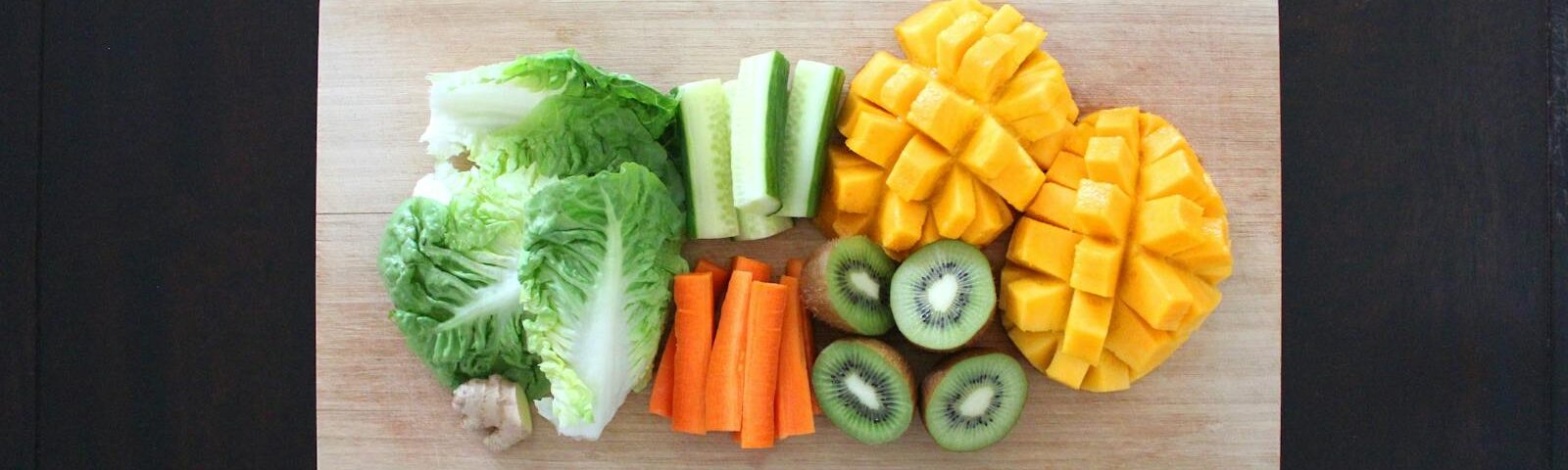 Fresh fruits and vegetables prepared for healthy salad on a wooden chopping board.