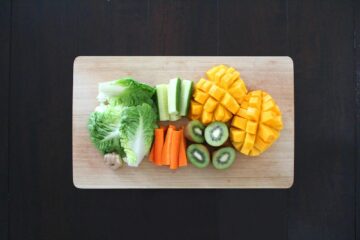 Fresh fruits and vegetables prepared for healthy salad on a wooden chopping board.