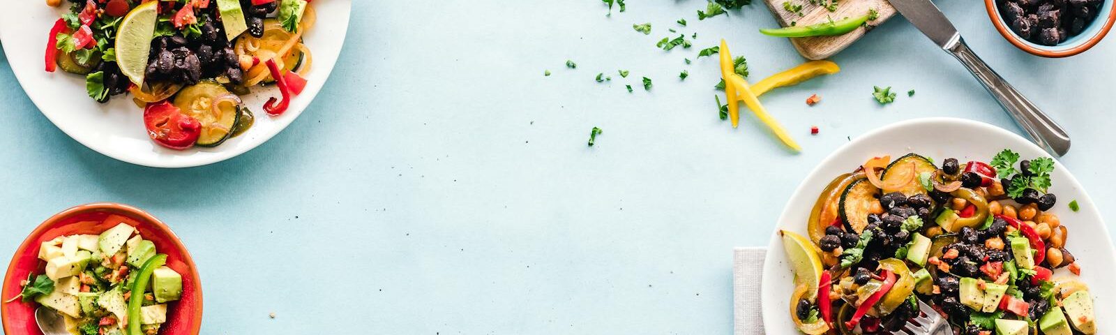 Colorful Mexican salad with avocado, black beans, and lime on a light blue surface.