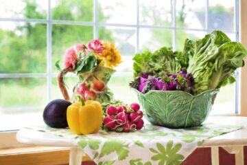 A vibrant display of fresh vegetables and flowers on a sunlit kitchen table by the window.