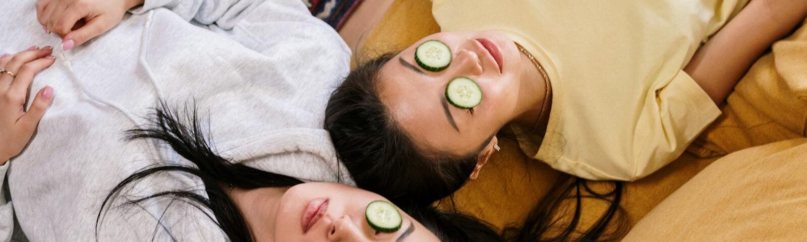 Two friends relaxing at home with cucumber masks in a cozy setting, enjoying a DIY skincare session.