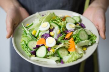 Freshly prepared salad with cucumber, lettuce, carrots, and egg slices presented on a plate.