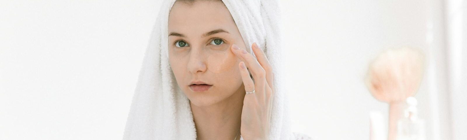 A woman in a bathrobe applying skincare products in a bright indoor setting.