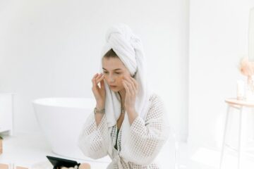 Woman in white bathrobe applying skincare in a bright bathroom. Perfect for wellness and beauty themes.