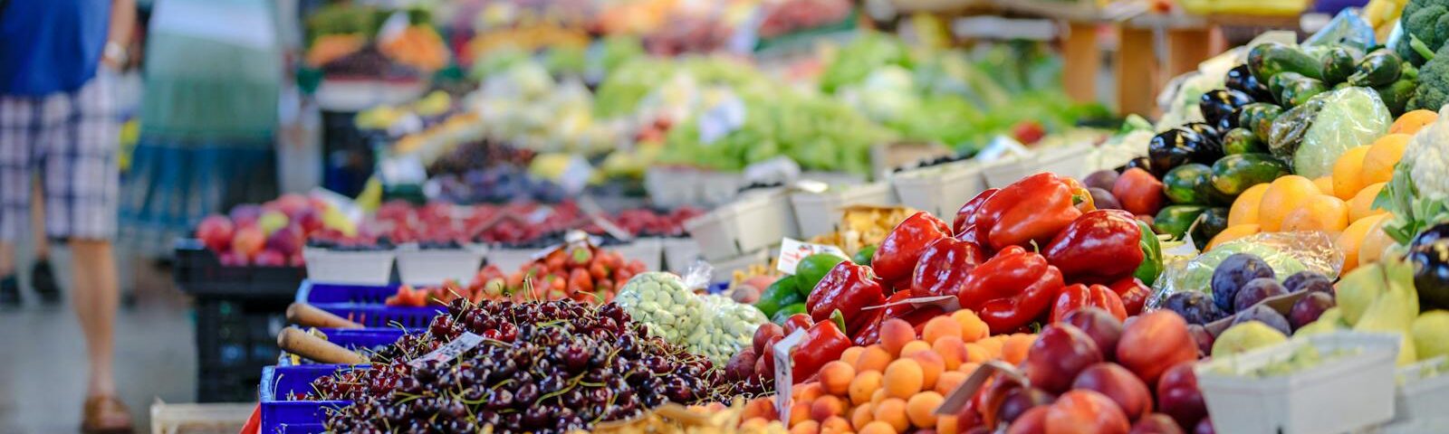 Colorful assortment of fresh fruits and vegetables in a bustling outdoor market scene.