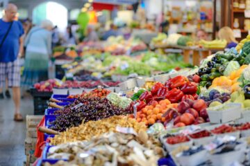 Colorful assortment of fresh fruits and vegetables in a bustling outdoor market scene.