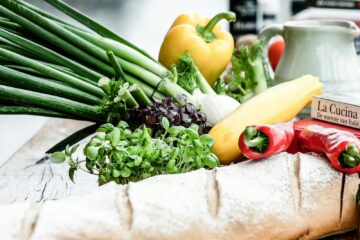 A vibrant assortment of fresh vegetables, herbs, and bread on a rustic surface, ideal for culinary scenes.